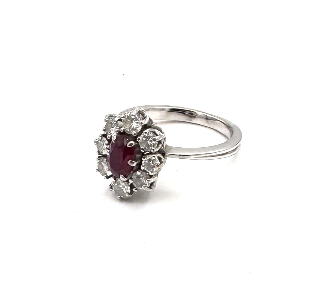 A RUBY AND DIAMOND CLUSTER RING A classic "Pompadour" design in 18k white gold: A timeless and highly elegant cluster ring, masterfully crafted in 18k white gold (750/1000). The design is centered upon a vibrant oval-cut ruby weighing approximately 0.75 carat. The gemstone displa