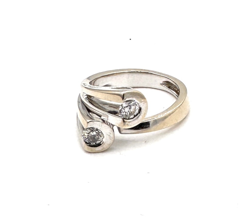 OTELINA – A DIAMOND TWO-STONE RING A bold sculptural "Toi et Moi" design in 18k gold: A modern and substantial dress ring by Otelina, masterfully crafted in 18k yellow gold (750/1000). The design features a broad, ergonomic band with a dynamic crossover silhouette, terminati