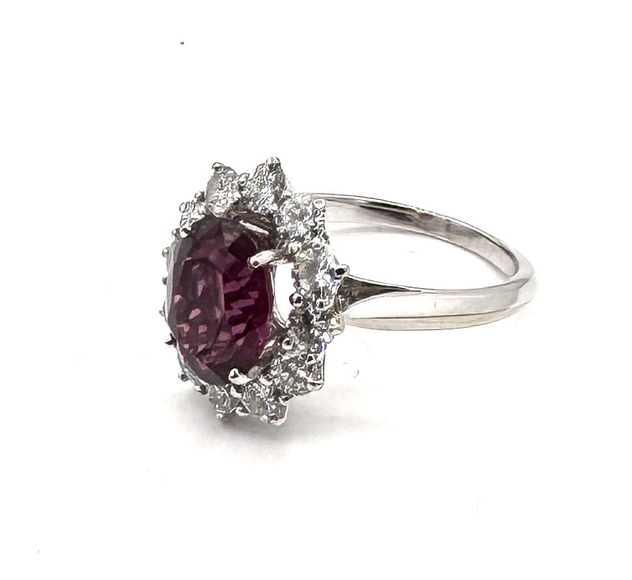 A STRIKING PINK SAPPHIRE AND DIAMOND CLUSTER RING A vibrant "Lady Di" inspired statement in 18k: A magnificent and feminine cocktail ring of classic "Oval Cluster" design, masterfully crafted in 18k white gold (750/1000). The centerpiece is a substantial oval-cut pink sapphire, measuring approxim