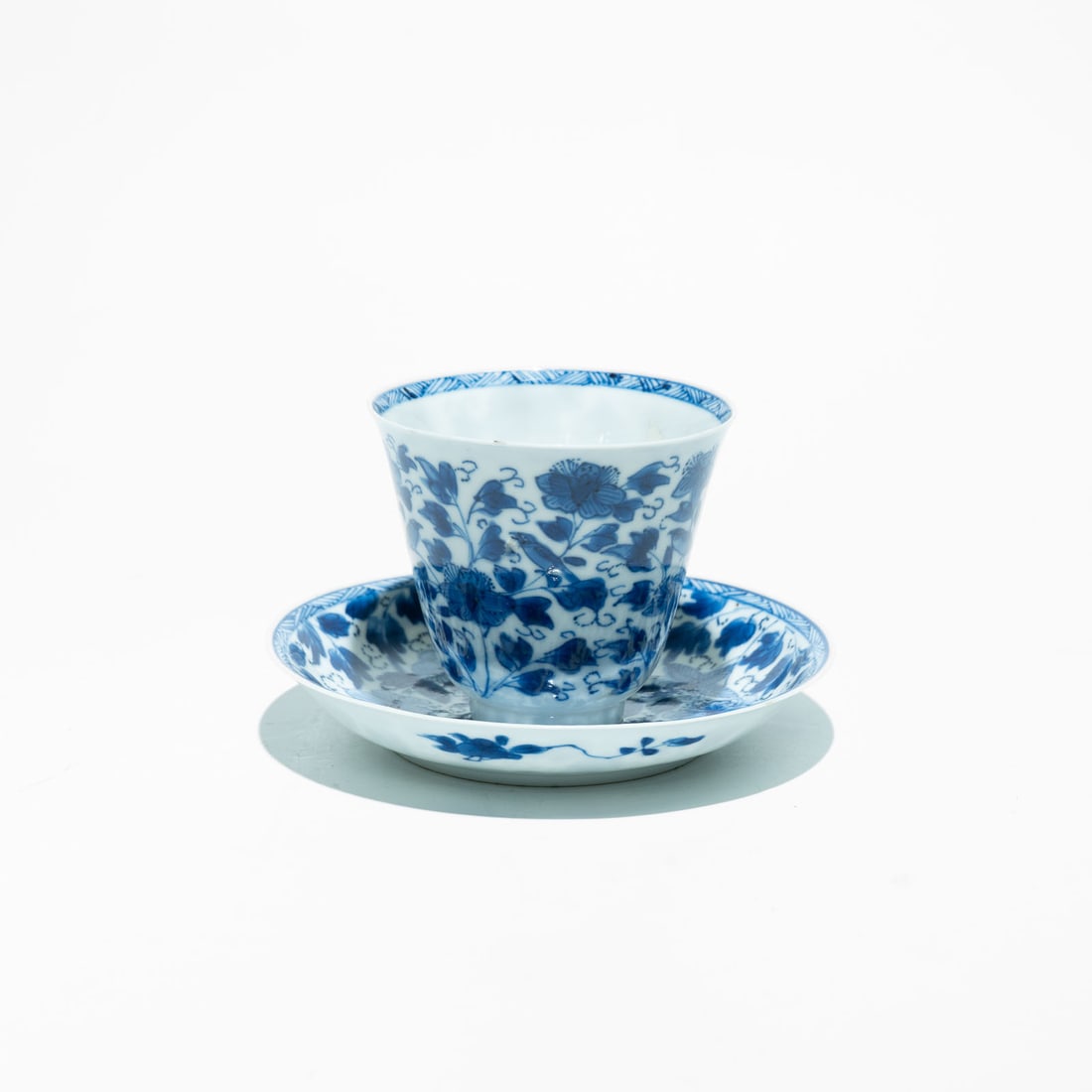 Chinese Export Porcelain, blue and white cup and saucer Kangxi Period(1662-1722): This piece is hand-painted with dense, vibrant cobalt blue floral scrolls. It features intricate peony and foliage designs, often including small birds or butterflies among the blossoms. The cup and s