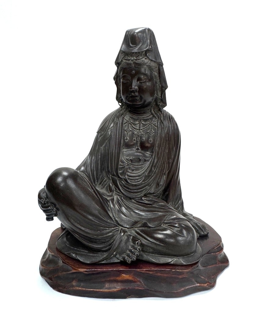 A Finely Cast Patinated Bronze Figure of Kannon Bosatsu Japan, Meiji Period (1868–1912): A cast bronze figure representing Kannon (Avalokiteshvara), the Bodhisattva of Infinite Compassion.The deity is depicted in the graceful posture of royal ease (lalitasana), seated