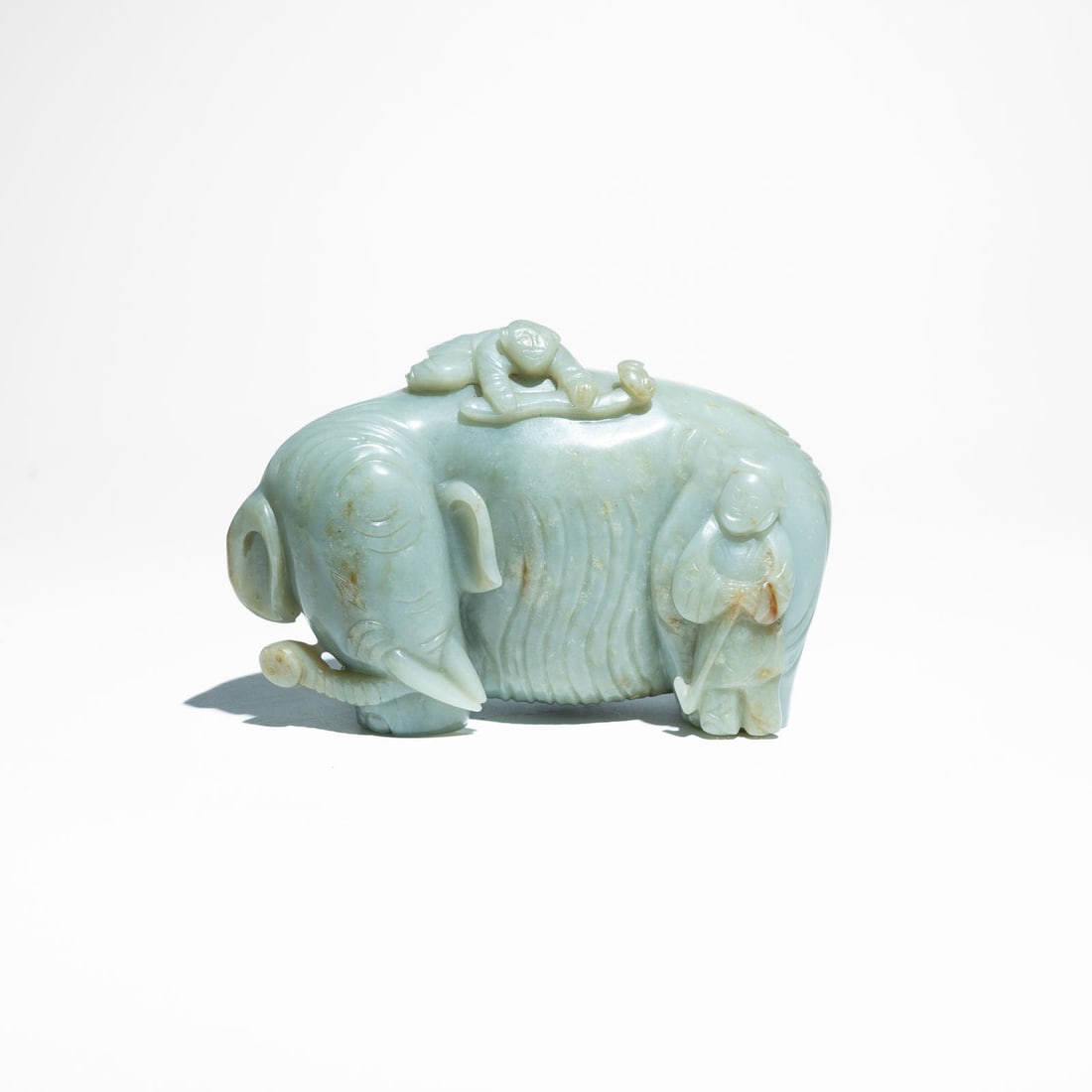 A carved Pale Celadon Jade Group of an Elephant and Attendants China, Republic Period (1912–: A charming pale celadon carved jade sculptural group depicting a caparisoned elephant flanked by attendants.The elephant is carved standing with its head turned slightly to the left, featuring heavy i