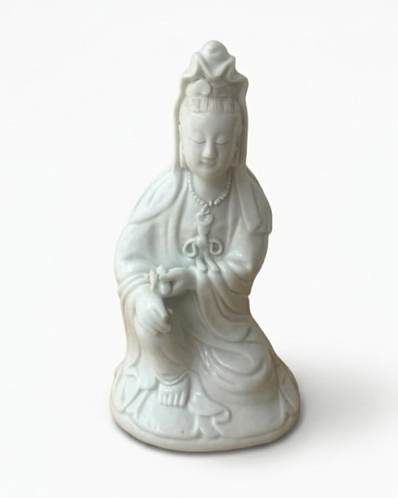 A Chinese Dehua 'Blanc de Chine' figure of Guanyin China, Qing Dynasty, 19th Century: A finely modeled white porcelain figure of Guanyin, the Bodhisattva of Compassion, depicted in a seated position of royal ease.The figure is draped in flowing robes that fall in elegant, rhythm