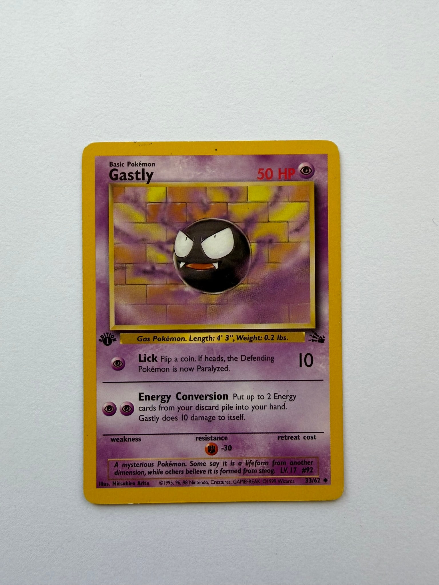 1999 Pokemon Gastly 33/62 Fossil 1st Edition: Vintage Gastly 33/62 from the 1999 Pokemon Fossil expansion. English 1st Edition non-holo uncommon featuring artwork by Mitsuhiro Arita. Ungraded with visible edge, corner and surface wear. Please rev