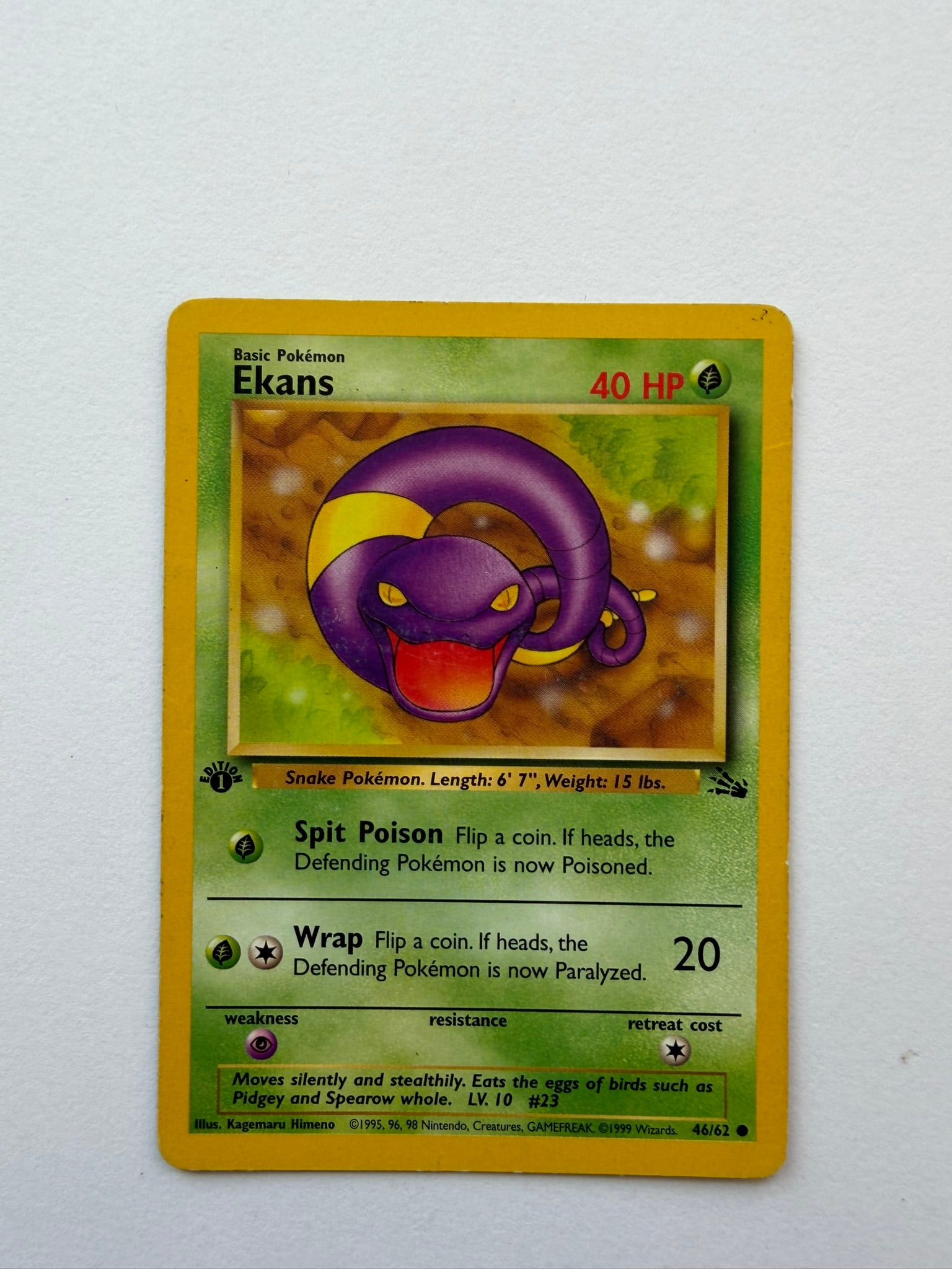 1999 Pokemon Ekans 46/62 Fossil 1st Edition: Vintage Ekans 46/62 from the 1999 Pokemon Fossil expansion. English 1st Edition common featuring artwork by Kagemaru Himeno. Ungraded with visible age-related edge and surface wear. Please review phot