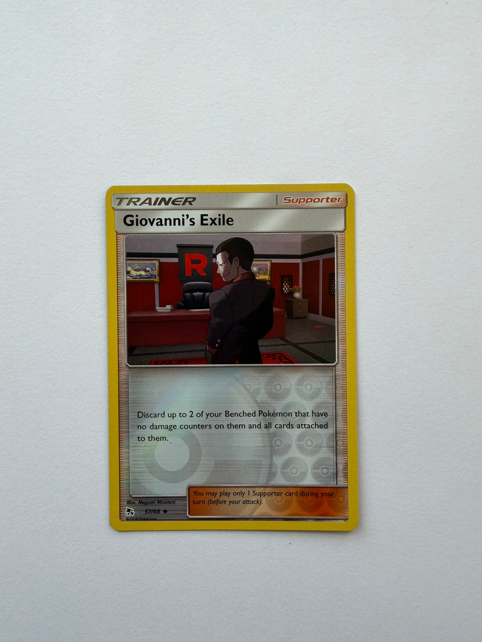 2019 Pokemon Giovanni's Exile 57/68 Hidden Fates Reverse Holo: Giovanni's Exile 57/68 reverse-holo Supporter card from the 2019 Pokemon Hidden Fates expansion. Features Team Rocket-themed artwork by Megumi Mizutani. Ungraded with visible edge and surface wear. Pl