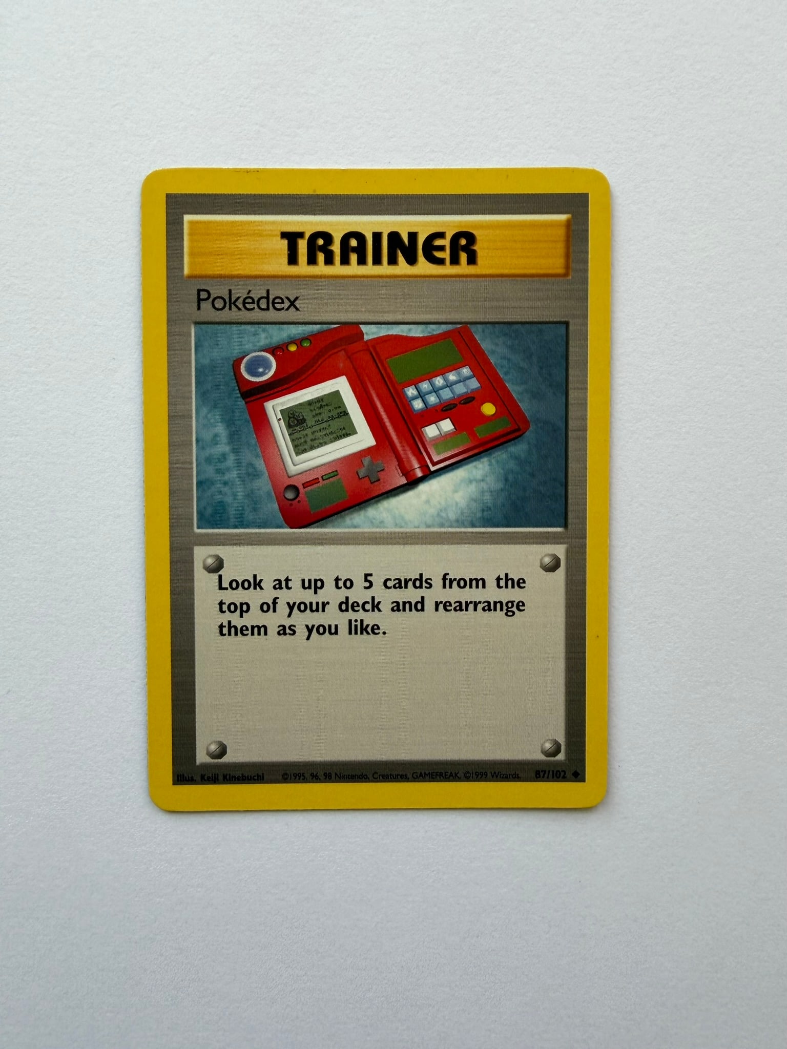 1999 Pokemon Pokedex 87/102 Base Set: Pokedex 87/102 Trainer card from the original 1999 Pokemon Base Set. Unlimited non-holo printing featuring Keiji Kinebuchi artwork. Ungraded with visible age-related edge and surface wear. Please revi