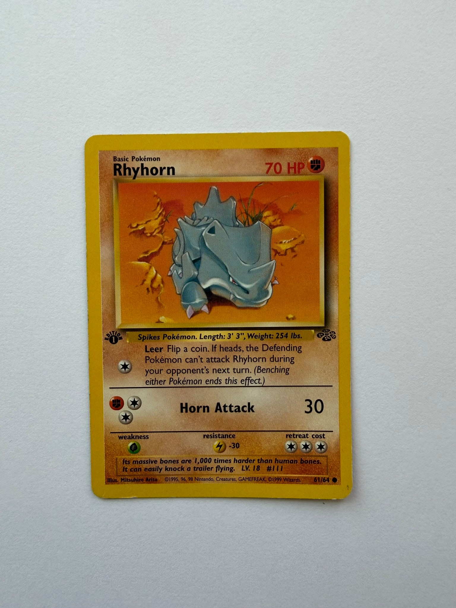1999 Pokemon Rhyhorn 61/64 Jungle 1st Edition: Rhyhorn 61/64 from the 1999 Pokemon Jungle expansion. First Edition non-holo card featuring classic Mitsuhiro Arita artwork. Ungraded with visible age-related edge and surface wear. Please review phot