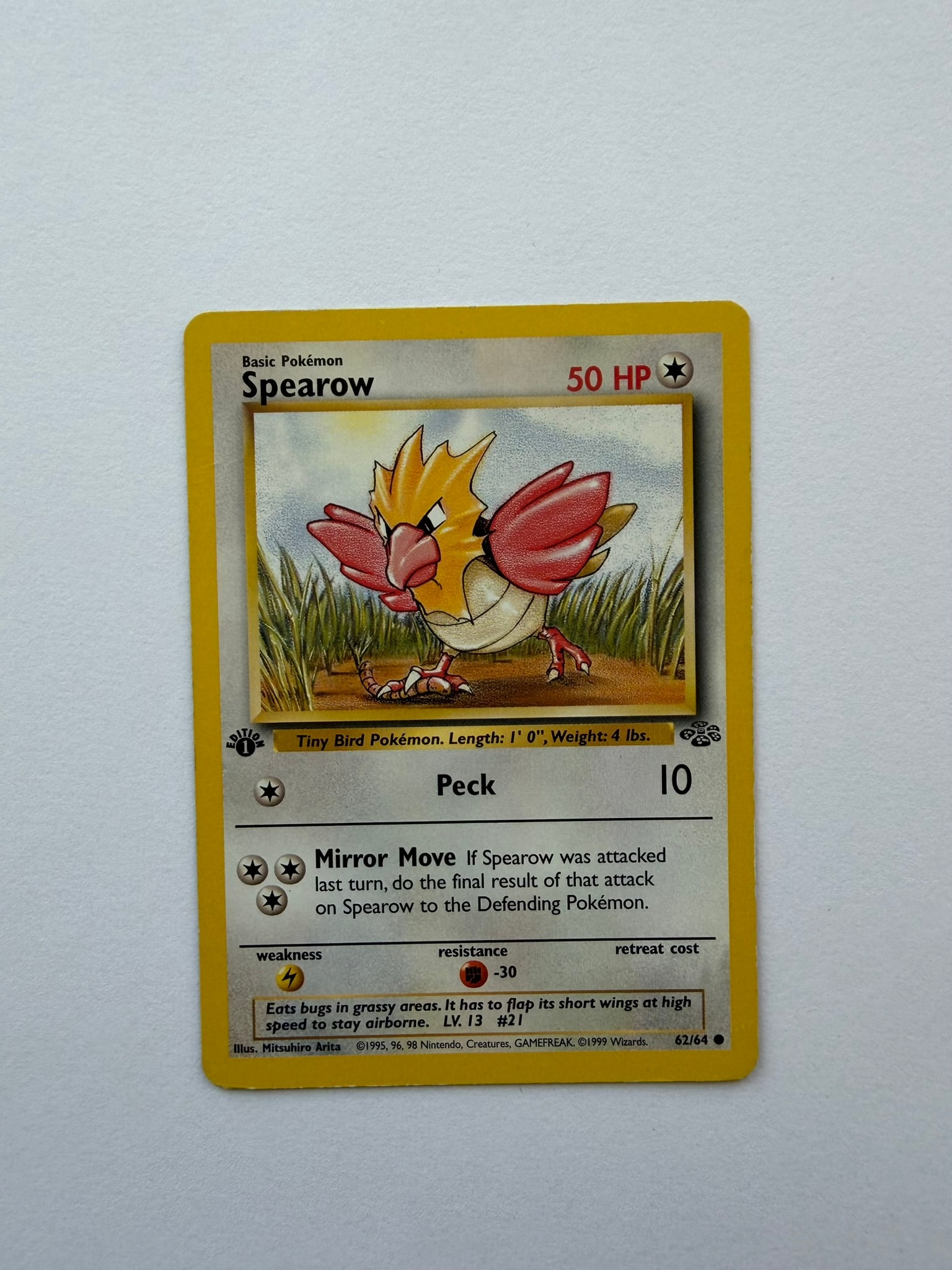 1999 Pokemon Spearow 62/64 Jungle 1st Edition: Spearow 62/64 from the 1999 Pokemon Jungle expansion. First Edition non-holo card featuring classic Mitsuhiro Arita artwork. Ungraded with visible age-related edge and surface wear. Please review phot