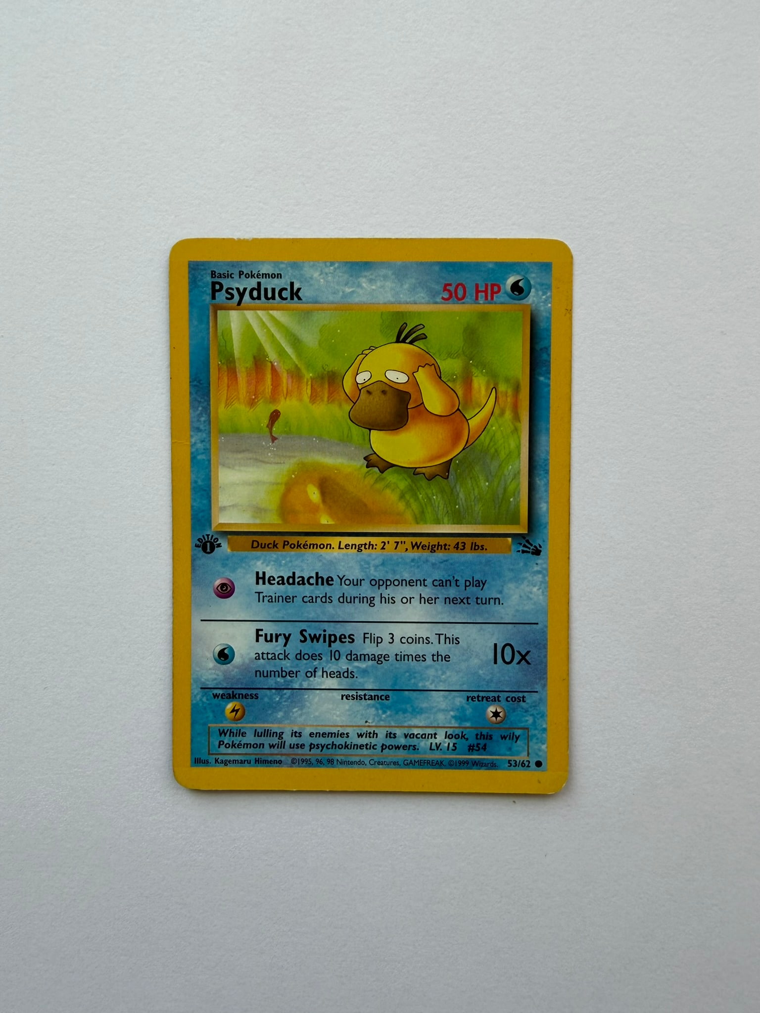 1999 Pokemon Psyduck 53/62 Fossil 1st Edition: Psyduck 53/62 from the 1999 Pokemon Fossil expansion. First Edition non-holo card featuring Kagemaru Himeno artwork. Ungraded with visible age-related edge and surface wear. Please review photographs 