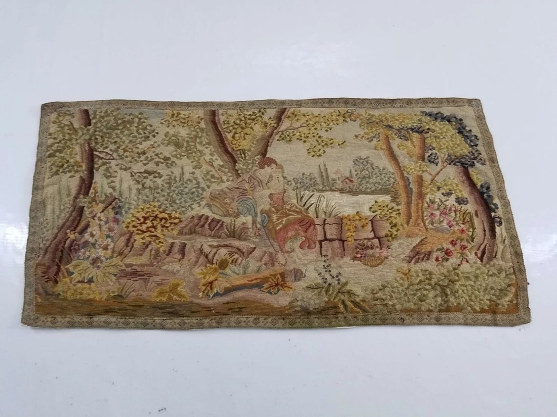 Antique French Romantic Scene Wall Tapestry, 128 x 64 cm: Antique French wall tapestry depicting a romantic pastoral scene with figures, trees, flowering plants, and a patterned border. The textile features a muted multicolor palette and decorative woven ima