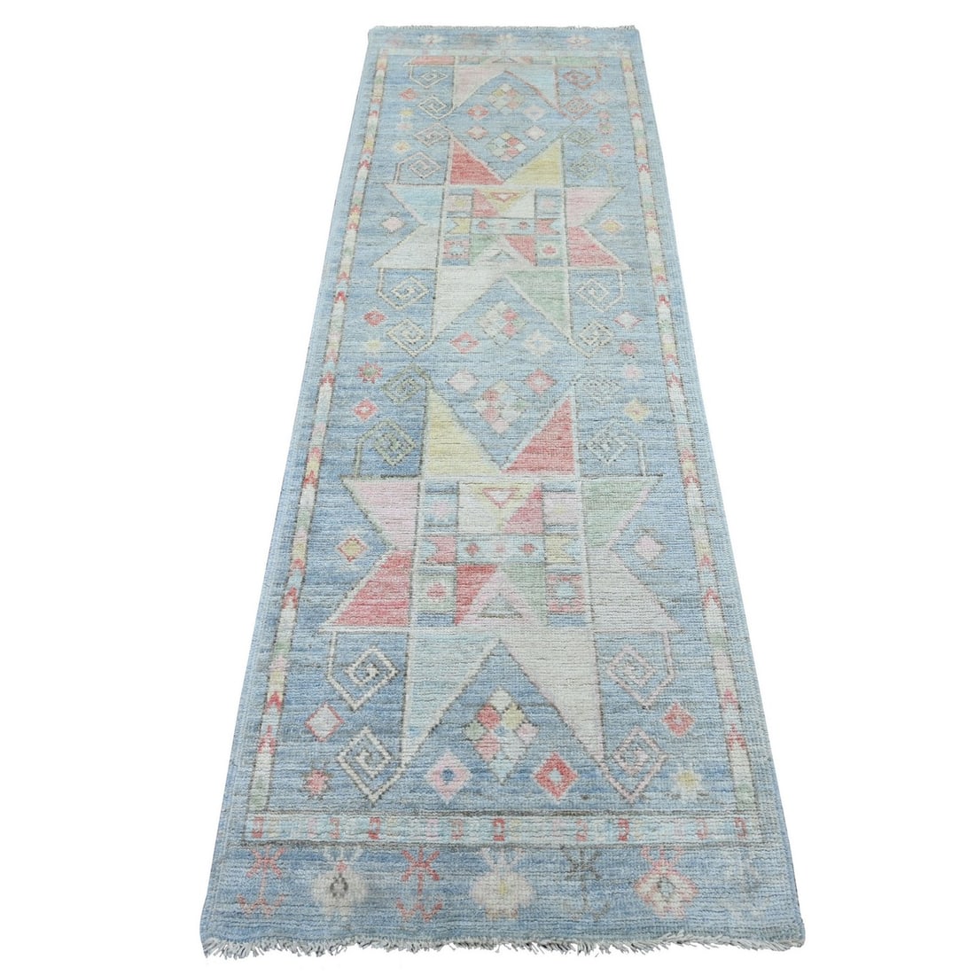 Blue Hand-Knotted Wool Runner Rug, Geometric Village-Inspired Design: Blue hand-knotted wool runner rug featuring a geometric village-inspired design with pastel blue, pink, cream, green, and yellow accents. The rug measures 2 ft 6 in by 8 ft 2 in and includes fringed e