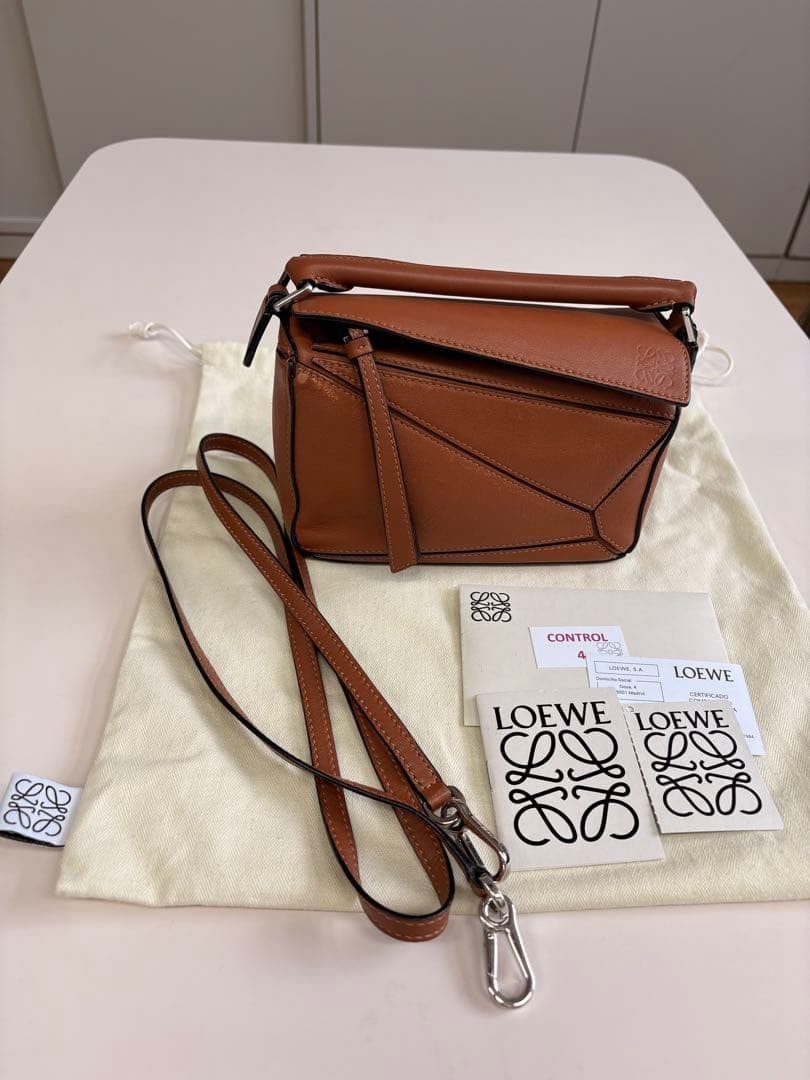 LOEWE Puzzle Mini Tan Calfskin Leather Crossbody Bag: LOEWE Puzzle Bag Mini crafted in tan calfskin leather with palladium-finish hardware. The design features geometric panel construction, an embossed Anagram motif, zip closure with calfskin pull, detac