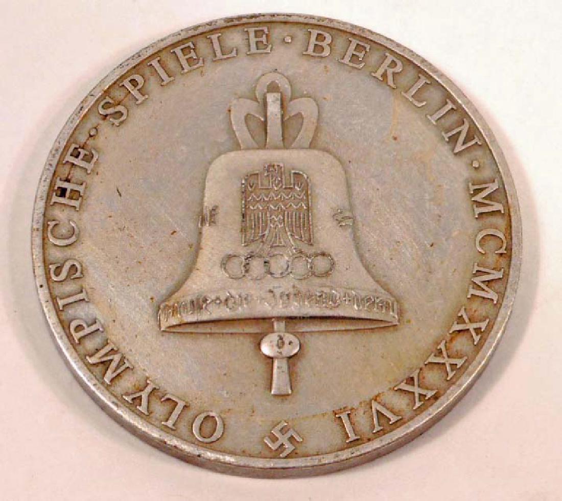 GERMAN NAZI SILVER BERLIN SUMMER OLYMPICS TABLE MEDAL: Measures 1 7/16" in diameter. The front shows a Greek Goddess holding a branch in One (1) hand and a wreath in the other. The reverse side shows the German WWII Olympic bell. Silver plated nickel cons