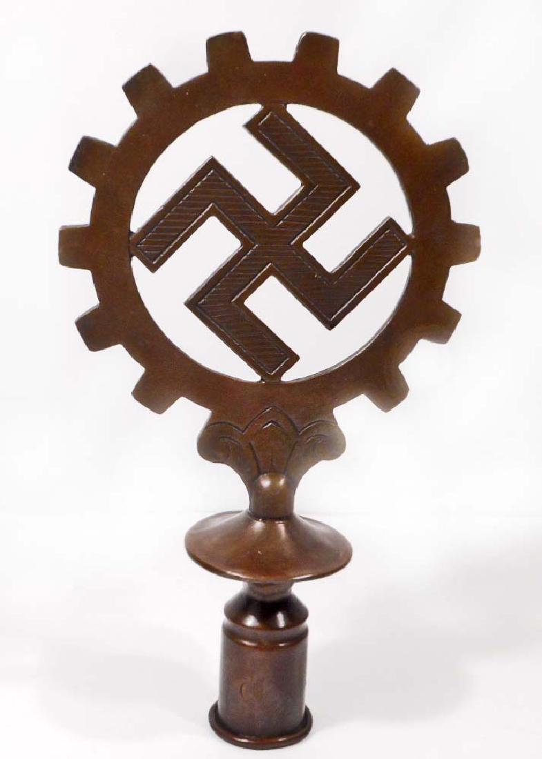 GERMAN NAZI DAF WORKERS FLAG POLE TOP: . Measures 5 3/8" wide by 9 3/4" tall. Shows a swastika in the center of the DAF cog wheel. Includes the base for mounting the flag pole into. One piece bronze construction