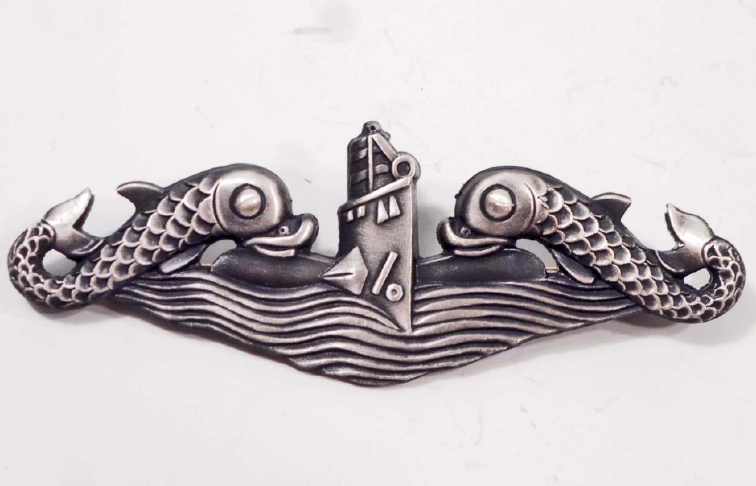 USN NAVAL SUBMARINE ENLISTED MANS BREAST BADGE: Measures 2 3/4" wide by 1" tall. The front shows a frontal view of a submarine flanked by a dolphin on each side. The reverse side is maker marked 'Gemsco' & 'Ster'. Has a thin horizontal pin back wit