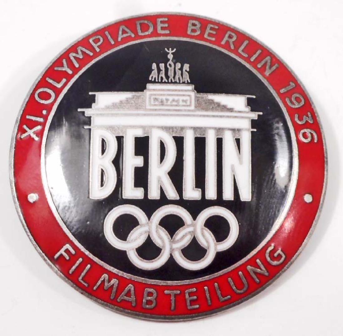 GERMAN 1936 BERLIN SUMMER OLYMICS FILM MAKER BADGE: Measures 1 1/2" in diameter. The reverse side is maker marked 'Rob Neff Berlin W 57'. Has a thin horizontal safety pin back. One piece nickel construction with red enamel.