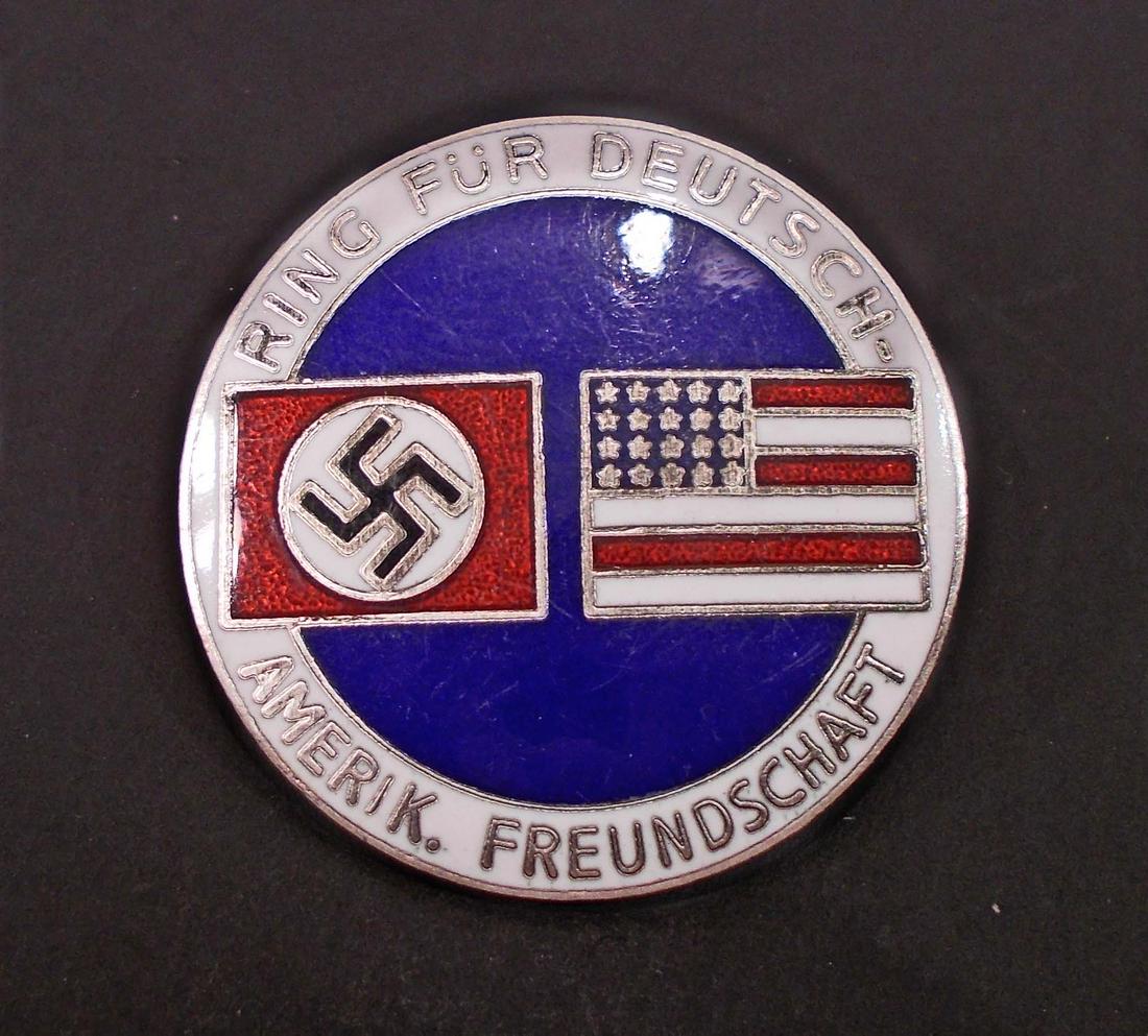 GERMAN AMERICAN BUND ENAMELED LAPEL BADGE: Measures 1 1/16" in diameter. The front shows a German swastika flag and an American flag. It reads 'Ring Fur Deutsche Amerik Freundschaft'. The reverse side is maker marked 'CTD'. Has a thin horizont