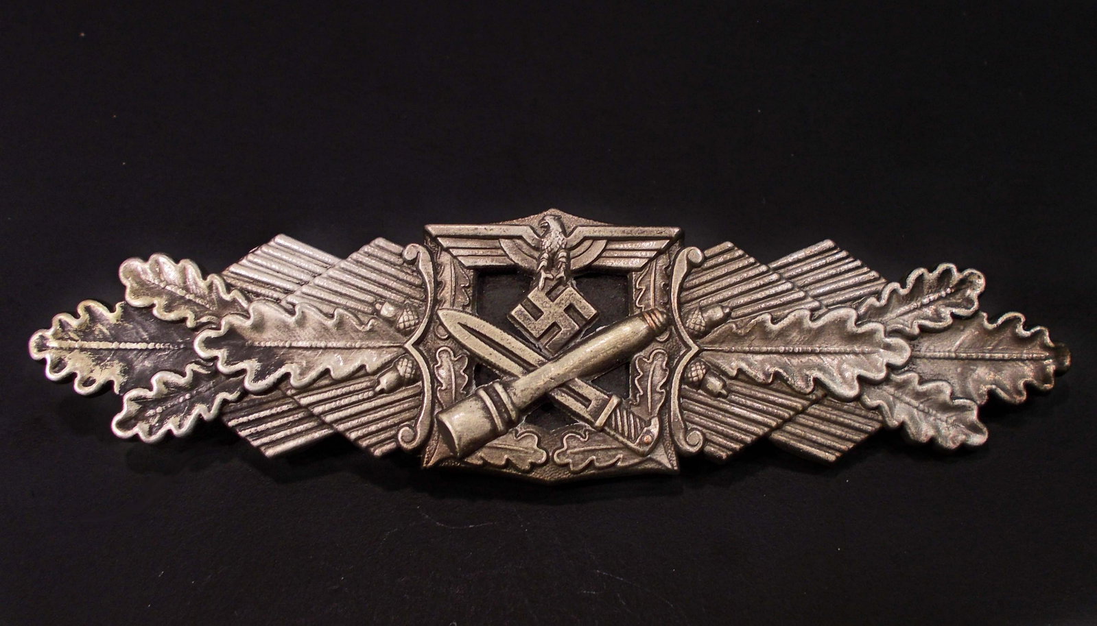 GERMAN NAZI ARMY SILVER CLOSE COMBAT CLASP: Front shows a German eagle with a crossed bayonet and stick grenade below. All Three (3) are flanded by oak leaves on each side. Reverse is maker marked Fec W E Peekhaus Berlin FLL. Has a wide horizon