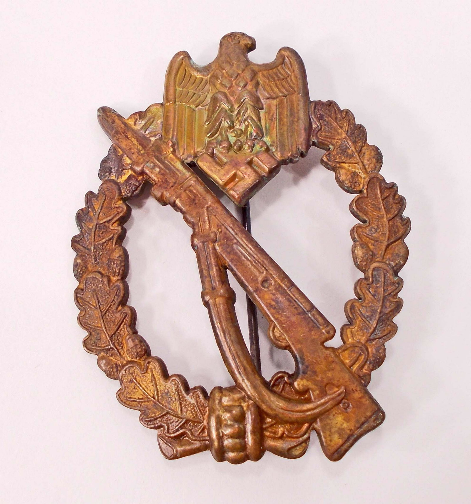 GERMAN NAZI ARMY BRONZE INFANTRY ASSAULT BADGE: Front shows a mauser K-98 rifle in the center with a German eagle above. Both are surrounded by an oval oak leaf wreath. Reverse side is maker marked GWL. Thin vertical pinback. Bronze vaulted consruc
