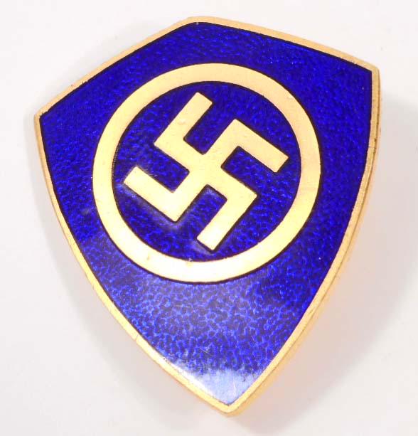 GERMAN NAZI SWASTIKA LAPEL BADGE: . Measures 1" wide by 1 1/8" tall. The front shows a swastika in the center surrounded by a circle in a shield shaped emblem. Has a thin vertical pin back. Brass construction with blue enamel.