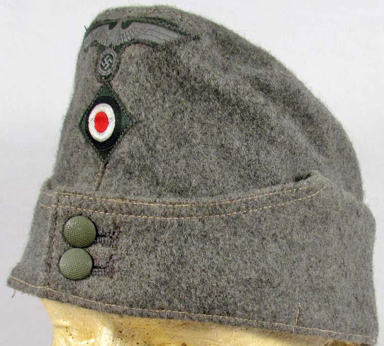 GERMAN NAZI ARMY EM OVERSEAS CAP: Maker marked Clemens Wagner Brausweig. Green wool construction. Has 2 piece bevo insignia this is machine sewn. For an enlisted man.