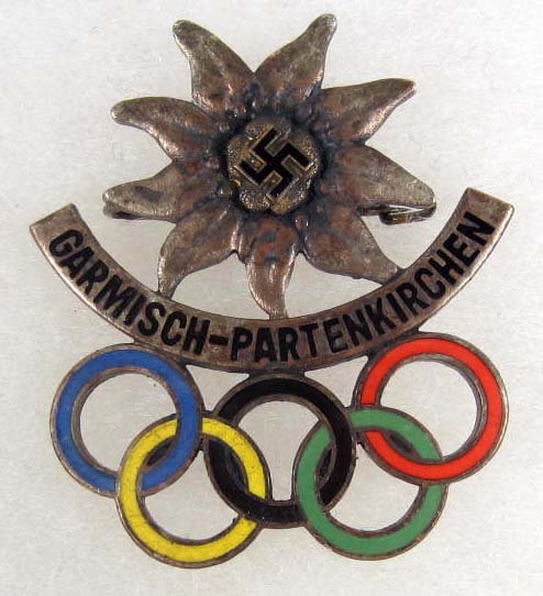 RARE GERMAN NAZI 136 GARMISCH WINTER OLYMPICS BADG: Maker marked Annetsberger Munchen. Pinback. Nickel and multi colored enamel construction. Has an eidelweiss w/ a swastika in the center. 'Below reads Garmisch - Partenkirchen and has the Olympic rings