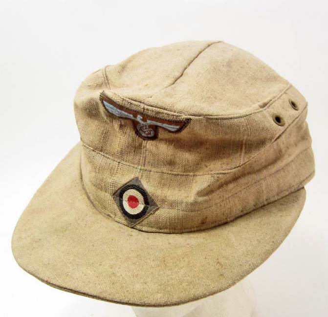 GERMAN NAZI ARMY AFRIKA KORPS TROPICAL EM M-41 CAP: hHas a blue AK bevo eagle and cockade machine sewn onto the front. The body is a tan khaki cotton material. The inside has the standard red cotton lining. There are four metal air vent grommets. For a