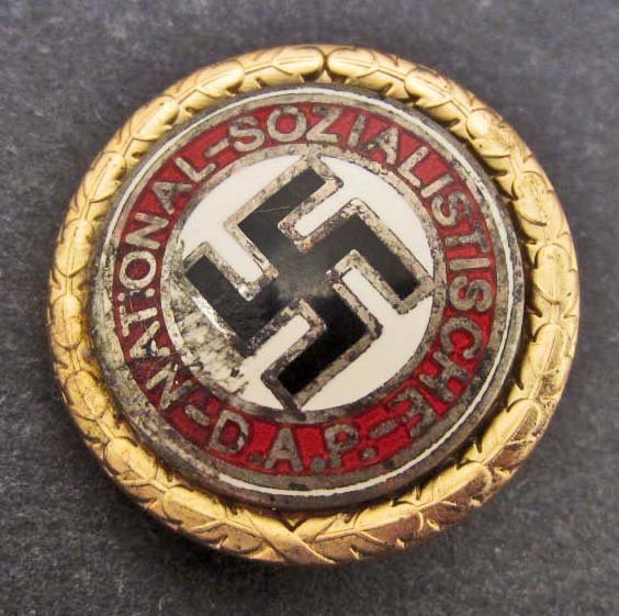 GERMAN NAZI NSDAP POLITICAL GOLDEN PARTY BADGE: Measures 1 ¼" in diameter. Has a wide vertical pin back. The reverse is marked Ges Gesch AH 30.1.1939. Has an enameled National - Sozialistische DAP Party Badge in the center. It is surrounded by a r