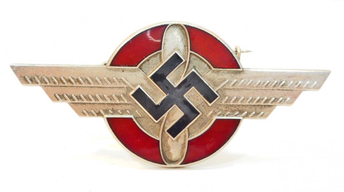 GERMAN NAZI NSFK/DLV GLIDER KORPS OFFICERS VISOR CAP: Measures 2-13/16" wide by 1-5/16" tall. Front shows a winged propeller with swastika in the center. The reverse side is maker marked RZM Ges Gesch. Horizontal pin back. Nickel construction with red an