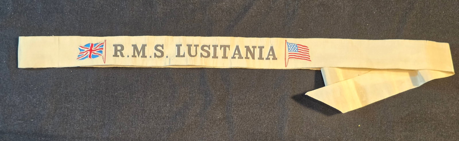Cunard R.M.S. Lusitania Hat Ribbon: Original Hat Ribbon, white. 50% of all proceeds from the sale of this lot will be donated to the Raise Your Banner Foundation, a Washington DC based non-profit whose mission is to break down the