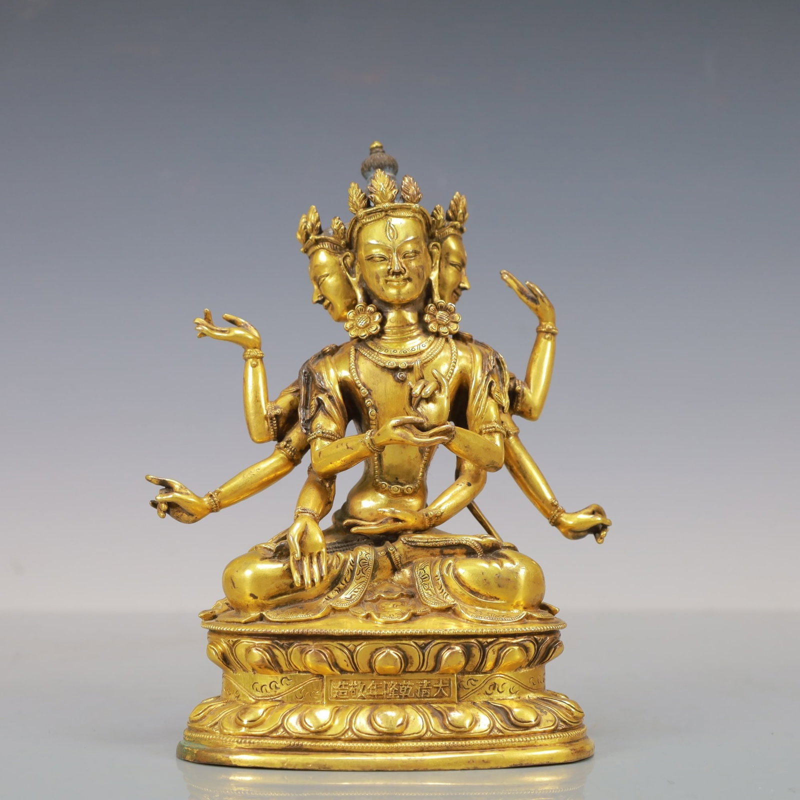 GILT-BRONZE THREE-HEADED GUANYIN FIGURE: Dimensions: 7 7/8 x 4 1/2 x 3 1/8 in; weight 1550 g This gilt-bronze three-headed Guanyin figure presents a striking fusion of spiritual symbolism and refined sculptural craftsmanship. The seated