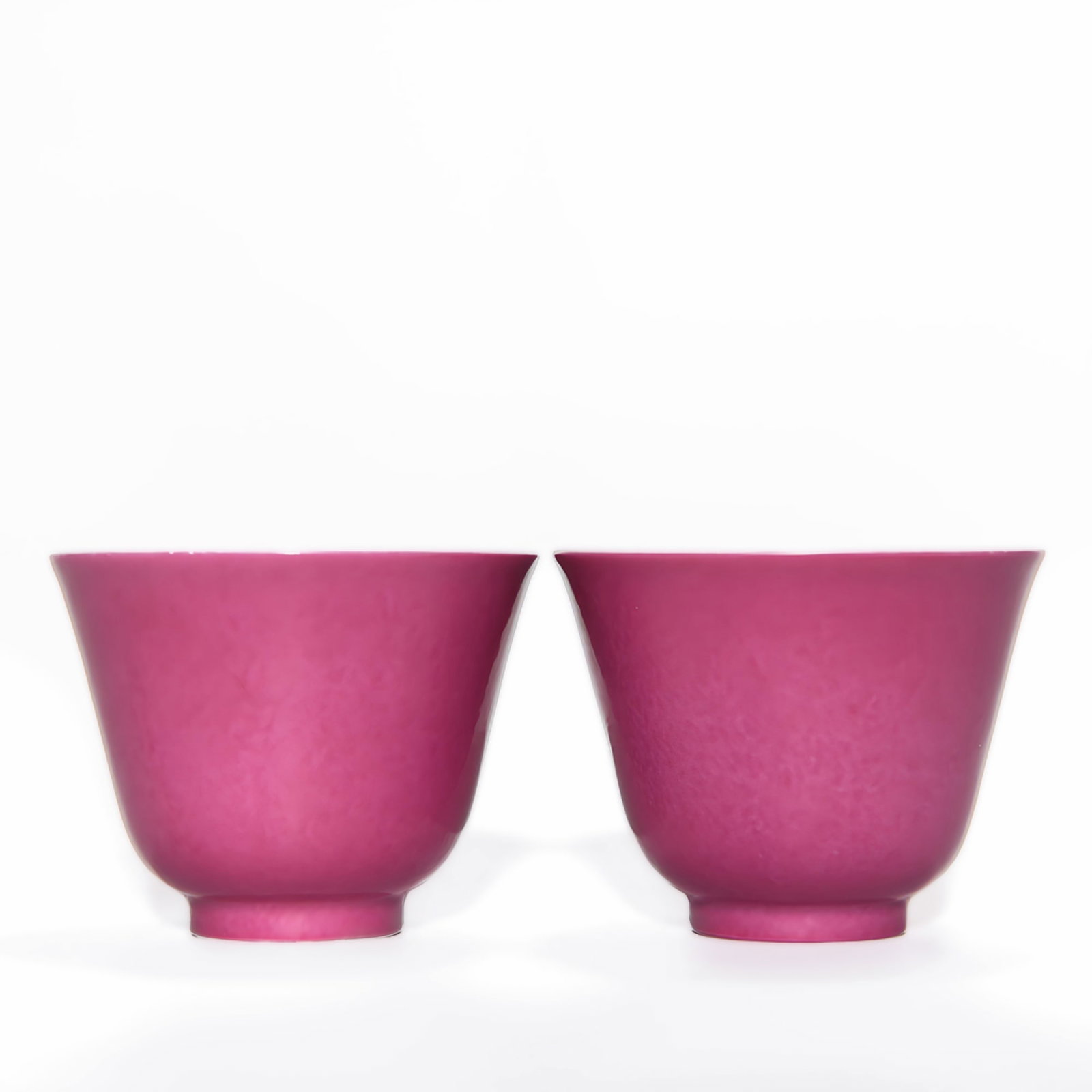 A PAIR OF KANGXI PERIOD MONOCHROME ROUGE-GLAZED CUPS: Dimensions: 2 x 2 5/8 in A pair of Chinese porcelain cups glazed in a rich rouge tone, each of gently flared form with a short foot. Dimensions (each): 2 1/16 x 2 9/16 in (5.2 x 6.5 cm).