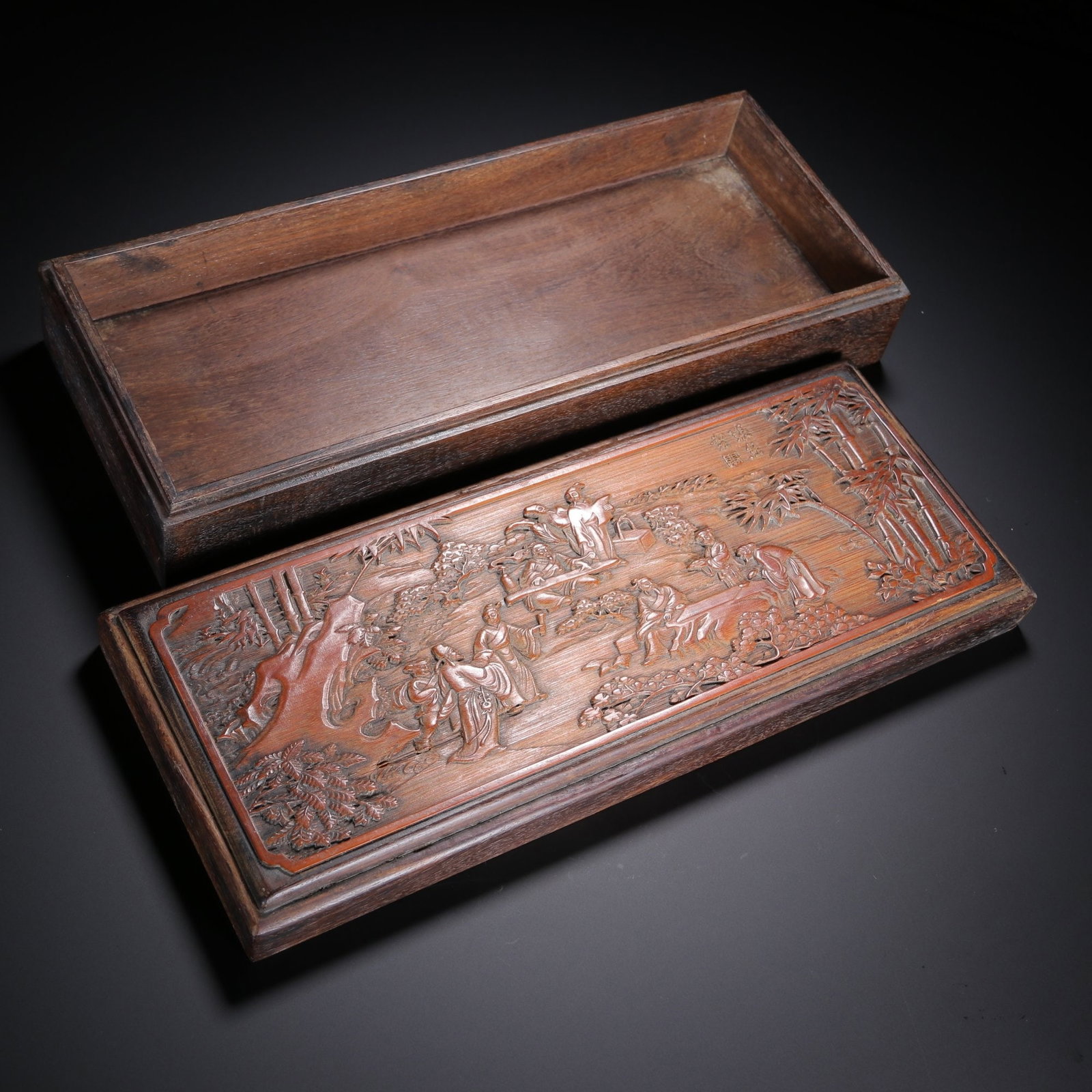 QING DYNASTY HONGMU BAMBOO-CARVED FIGURAL BOX: Dimensions: 11 5/8 x 4 3/4 x 2 1/2 in; weight 763.6 g This Qing dynasty hongmu bamboo-carved figural box presents a refined combination of hardwood craftsmanship and intricate narrative carving. The