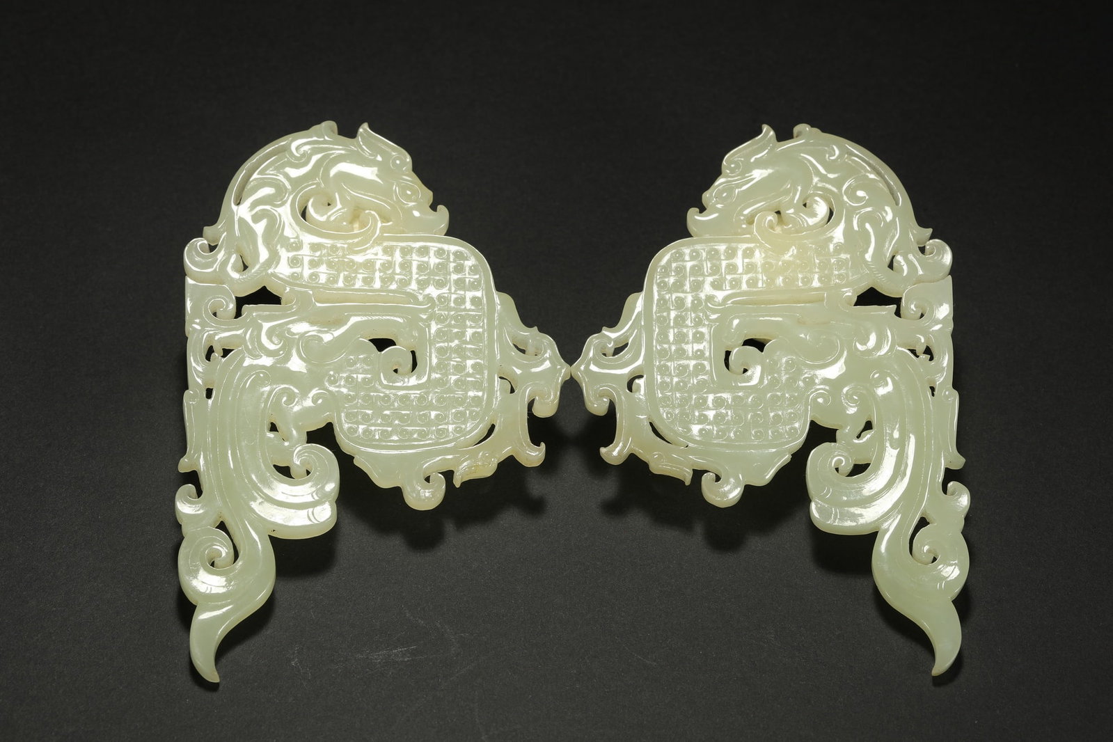 HETIAN JADE DRAGONS, A PAIR: Dimensions: 4 1/8 x 2 3/4 in; weight 91 g This pair of Hetian jade dragons presents a powerful sculptural character through expressive carving and balanced symmetrical composition. The dragon forms