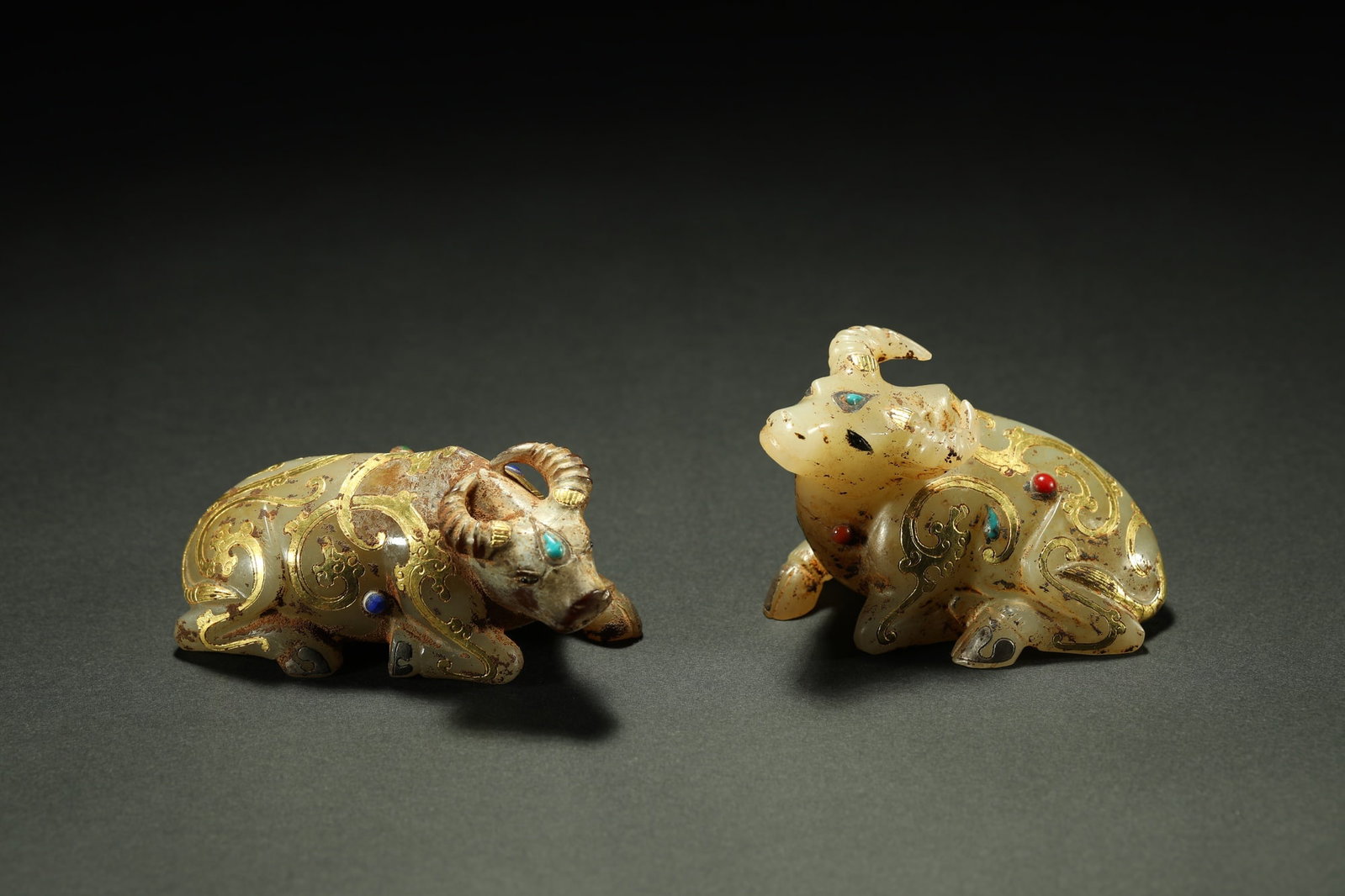 HETIAN JADE GILT BULLS, A PAIR: Dimensions: 2 3/4 x 1 3/4 in; weight 260 g This pair of Hetian jade gilt bulls presents a charming combination of refined jade carving and auspicious symbolism. The recumbent bulls are rendered with