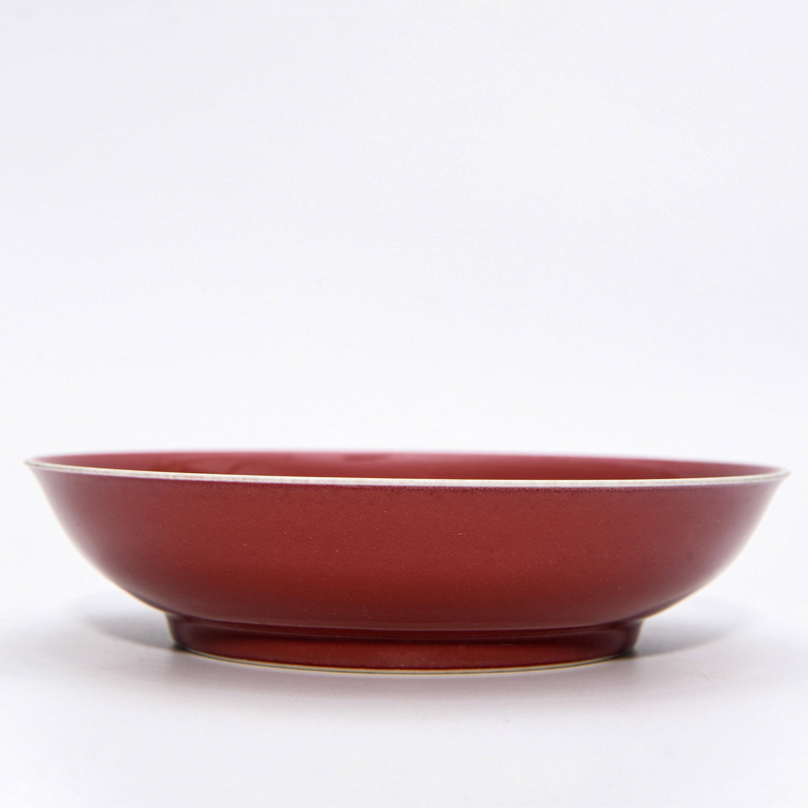 XIANFENG RED-GLAZED DISH: Dimensions: 1 3/4 x 7 3/8 in This Xianfeng red-glazed dish demonstrates a striking minimalist elegance through its luminous monochrome surface and refined proportions. The shallow circular form