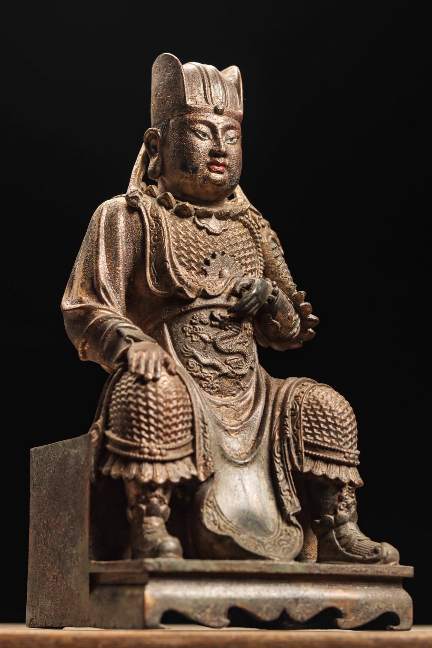 A GILDED BRONZE STATUE OF EMPEROR ZHENWU FROM THE QING DYNASTY: Weight:508g(1.12lb)H:25cm(9.84in)W:12cm(4.72in)T:12cm(4.72in)This martial deity statue sits solemnly on a square pedestal, wearing an official crown with dignified gentle facial features and remaining
