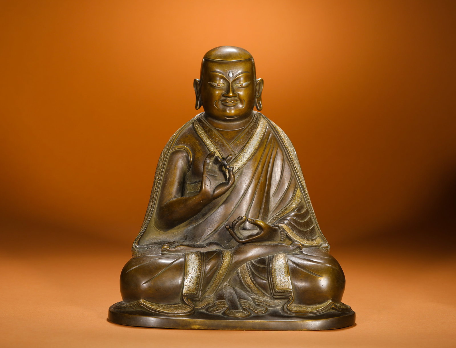BRONZE SEATED FIGURES OF MASTERS FROM THE QING DYNASTY: Height:24cm(9.45in) Width:22cm(8.66in) Weight:5400g(11.90lb)Qing Dynasty bronze lama statue with partial silver inlay, cast from brass. Silver wire inlay decorates the robe rims and folds. The master 