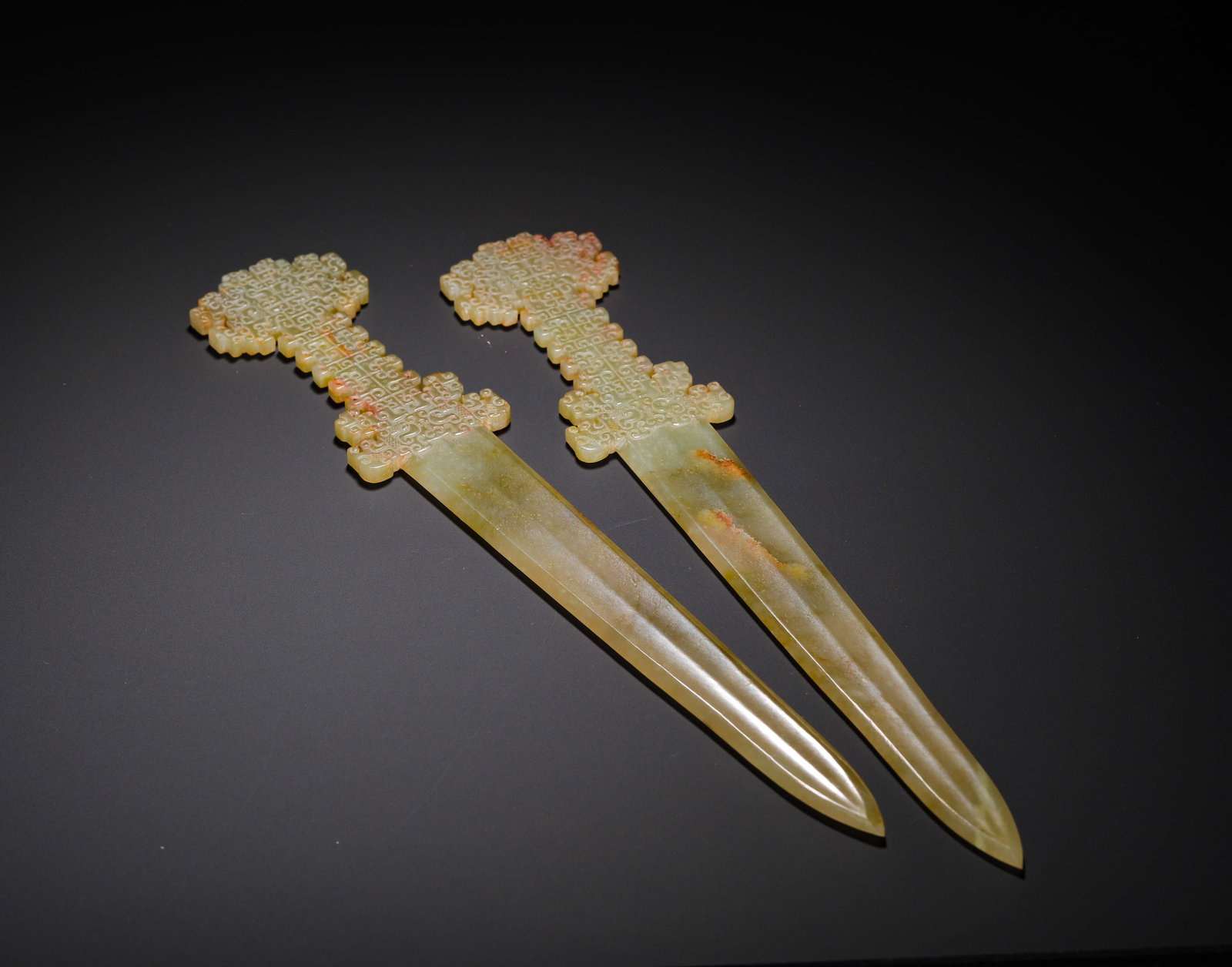 A PAIR OF YELLOW JADE SWORDS FROM THE HAN DYNASTY: Long:33.5cm(13.19in) Width:6cm(2.36in) Weight:270g(0.60lb)A pair of Han Dynasty yellow jade swords carved with chi dragon patterns on hilts, inscribed golden bird-worm seal script on blades, ritual ja