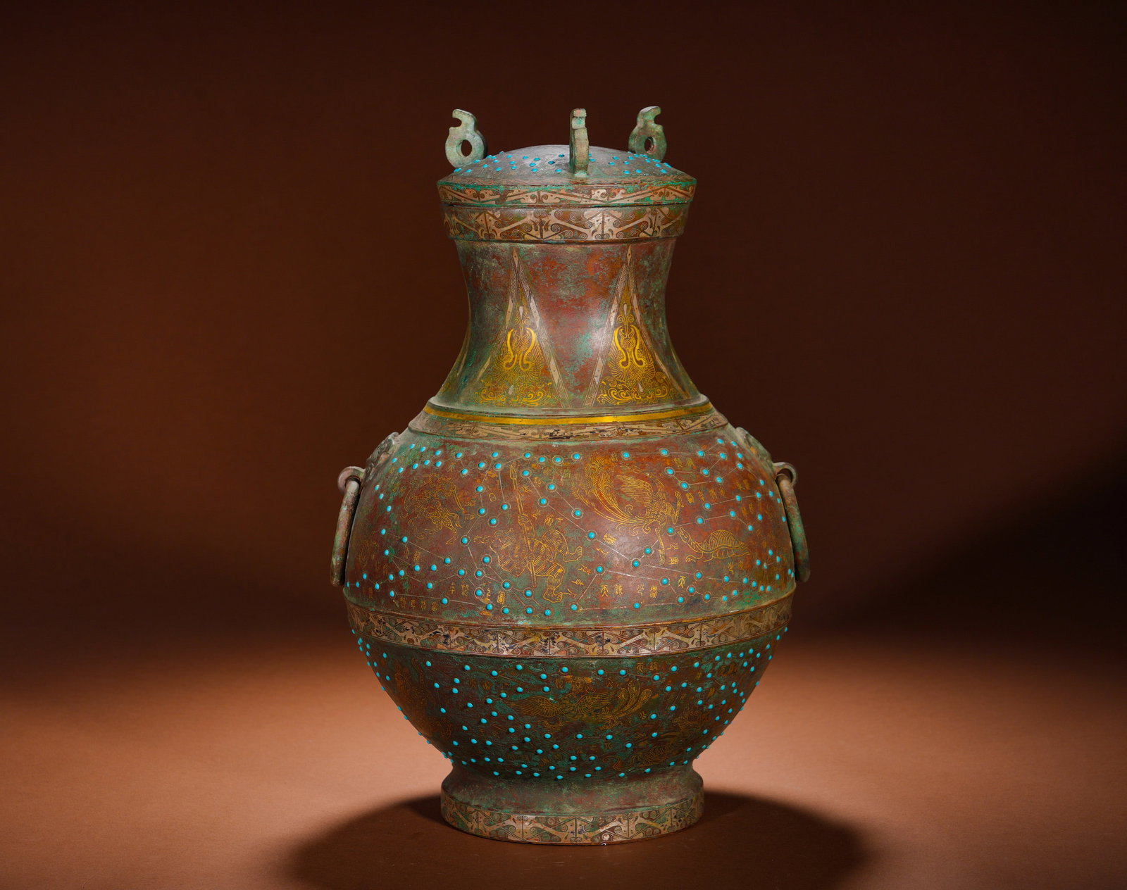 BRONZE CAULDRON WITH INLAID GOLD AND SILVER AND TURQUOISE CONSTELLATIONS AND DIVINE BIRDS: Height:35cm(13.78in) Width:24cm(9.45in) Weight:4880g(10.76lb)Cast bronze covered hu vessel with slender neck, bulbous belly and ring foot. The lid has twin curved knobs, and animal-head ring handles a
