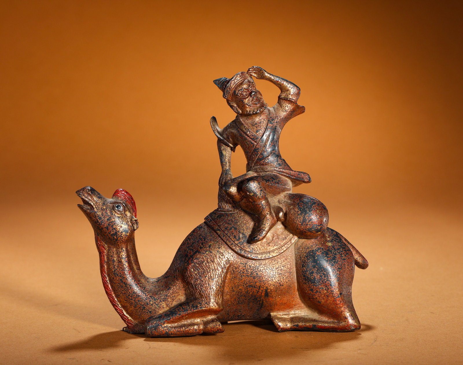 BRONZE LACQUERED GOLDEN HU ON A CAMEL FROM THE MING DYNASTY: Height:15cm(5.91in) Width:17cm(6.69in) Weight:1070g(2.36lb)Lacquered gilt bronze ornament of a Hu merchant riding camel. Bronze core with black lacquer, worn gold and red patina. The foreign merchant 