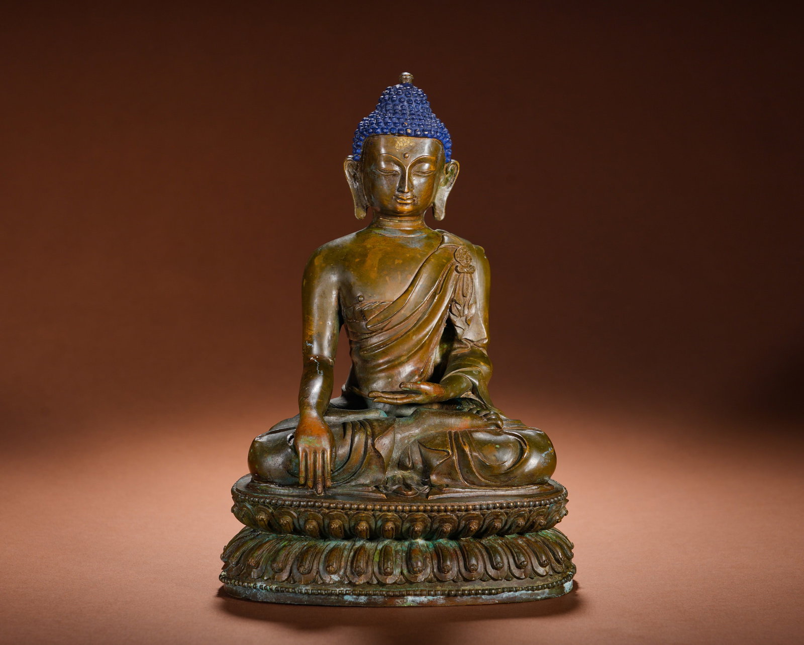 A BRONZE STATUE OF SAKYAMUNI ATTAINING ENLIGHTENMENT FROM THE QING DYNASTY: Height: 26cm(10.24in), Width: 17cm(6.69in), Weight: 2490g (5.490lb)Cast in fine bronze during the Qing Dynasty with natural aged patina, the Buddha??s spiral ushnisha is fully pigmented in mineral blu
