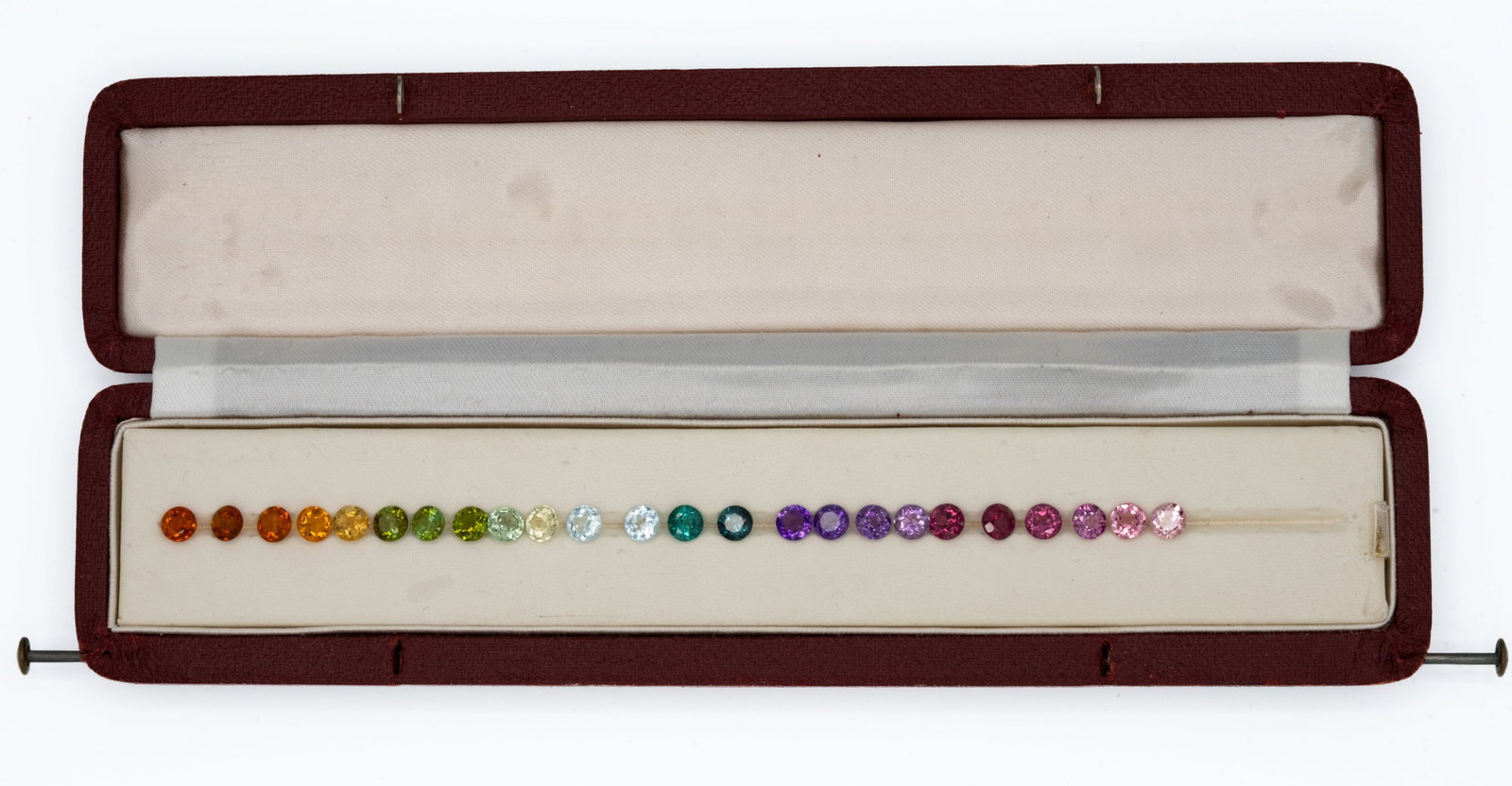 24pc Multi-Color 5.5mm Gem Suite: Color-graduated suite of 24 calibrated round faceted gemstones, each approximately 5.5 mm, presented in a long burgundy jewelry case. Desk refractive-index spot checks identify a mixed-species parcel