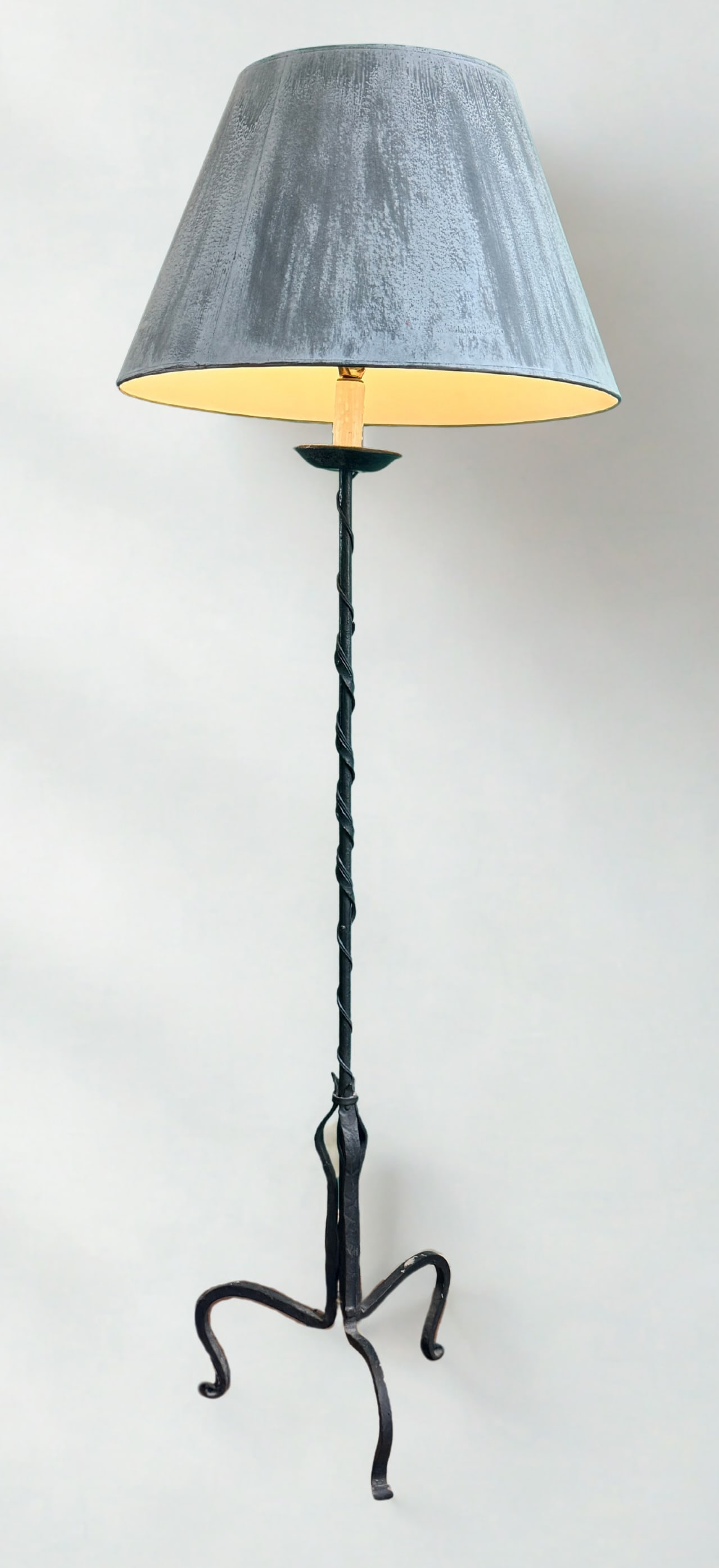 Vintage Wrought Iron Floor Lamp: Vintage Wrought Iron Floor Lamp, 1960s. Mid Century This lamp features tripod scroll legs, a hand-forged twisted stem and a gray tapered fabric shade. Dimensions: 23" x 23" x 66" Provenance: Private c