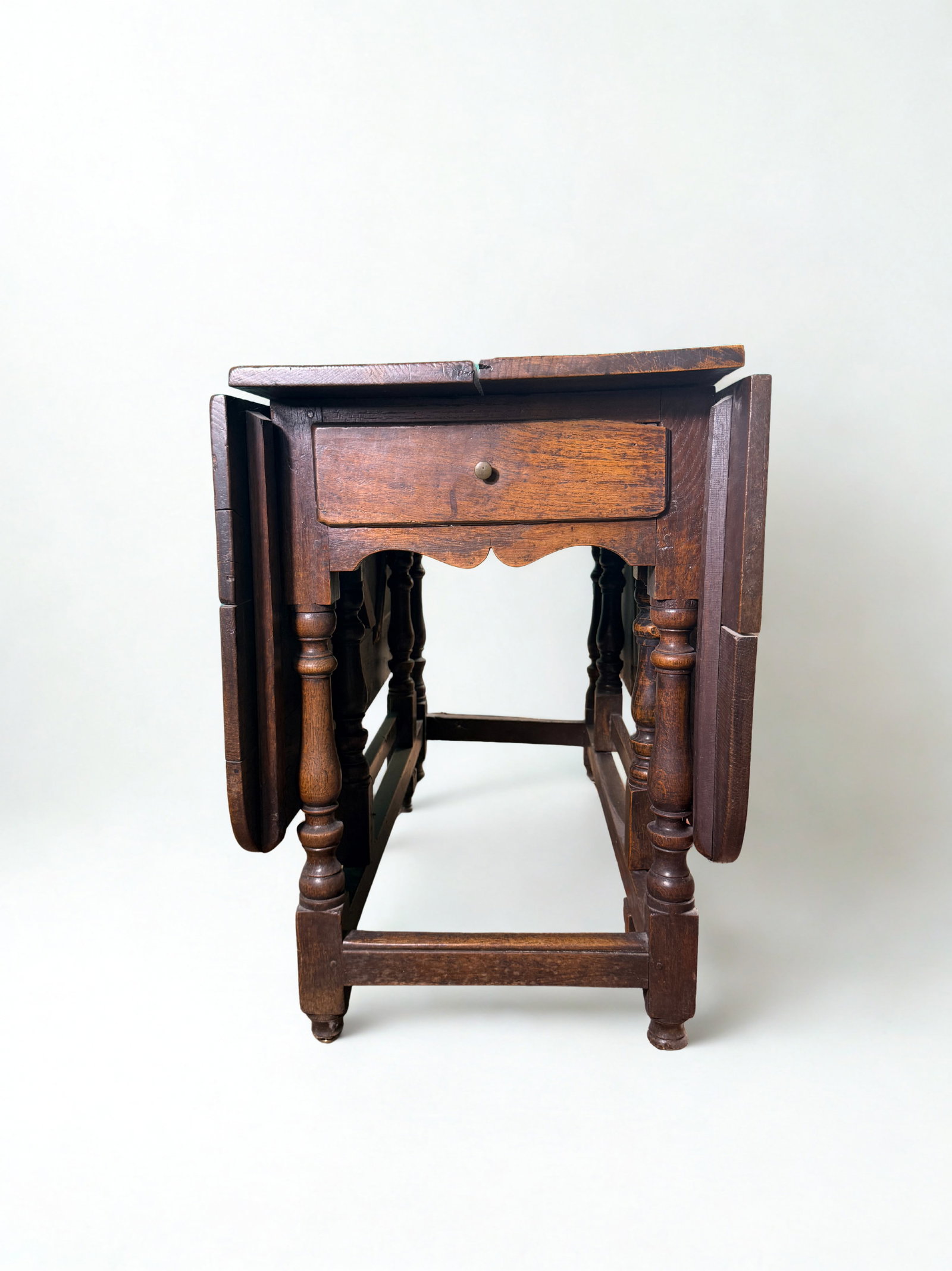 18th-Century English Oak Gate-Leg Table & Drawer: 18th century English oak gate-leg table, rich with period character and beautiful turned details. The top features a classic drop-leaf design, allowing each side to be extended and supported by elegan