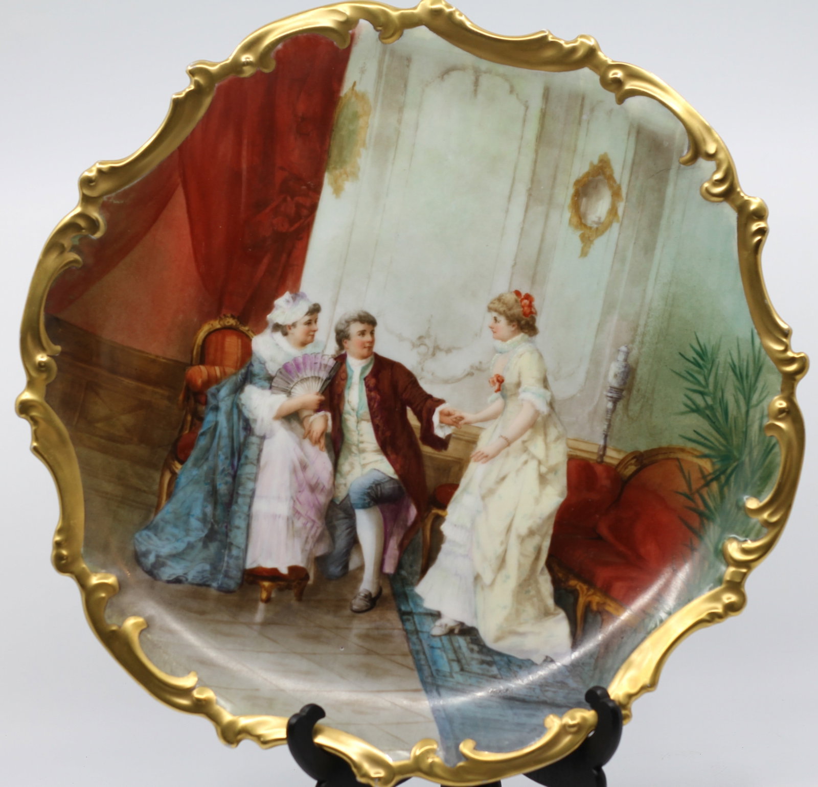 MUVILLE, FRENCH PORCELAIN CHARGER, C 1900: A French porcelain charger, circa 1900. Hand painted image to the basin depicting an interior salon scene. Fired gold scroll form border. Artist's signature "Muville" to the lower right.