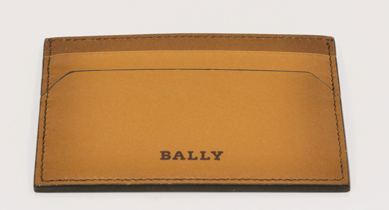 Bally Brown Leather Card Holder, Made in Italy: Bally slim card holder crafted in warm brown leather with darker brown edging and tonal stitching. The minimalist rectangular design features exterior card slots on both sides and a central open compa