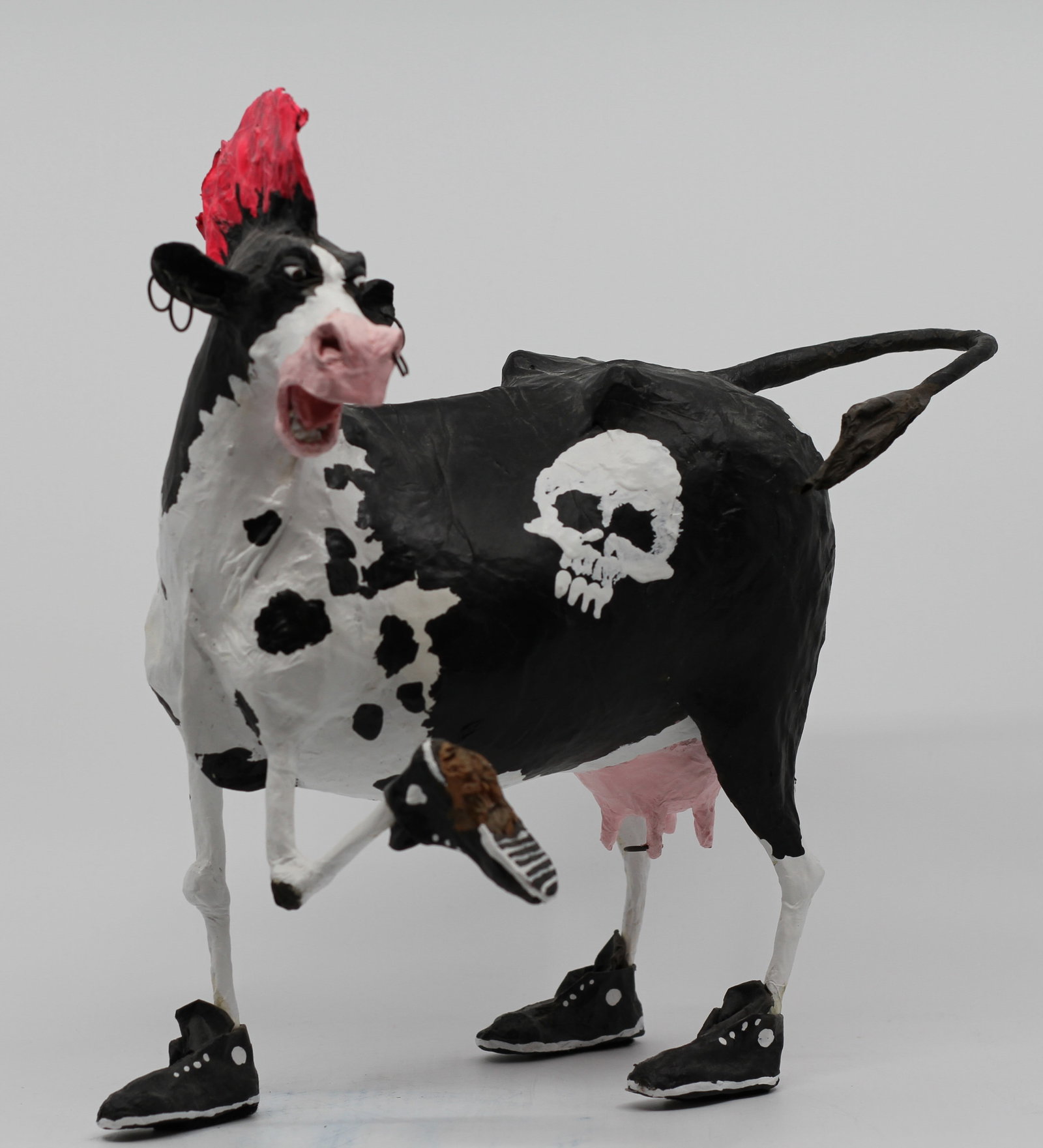 Contemporary Folk Art Punk Cow Sculpture with Red Mohawk and Skull Motif: Whimsical hand-formed and hand-painted mixed-media sculpture depicting a black-and-white cow with an exaggerated expression, bright red mohawk, multiple hoop-style piercings, black high-top sneakers, 