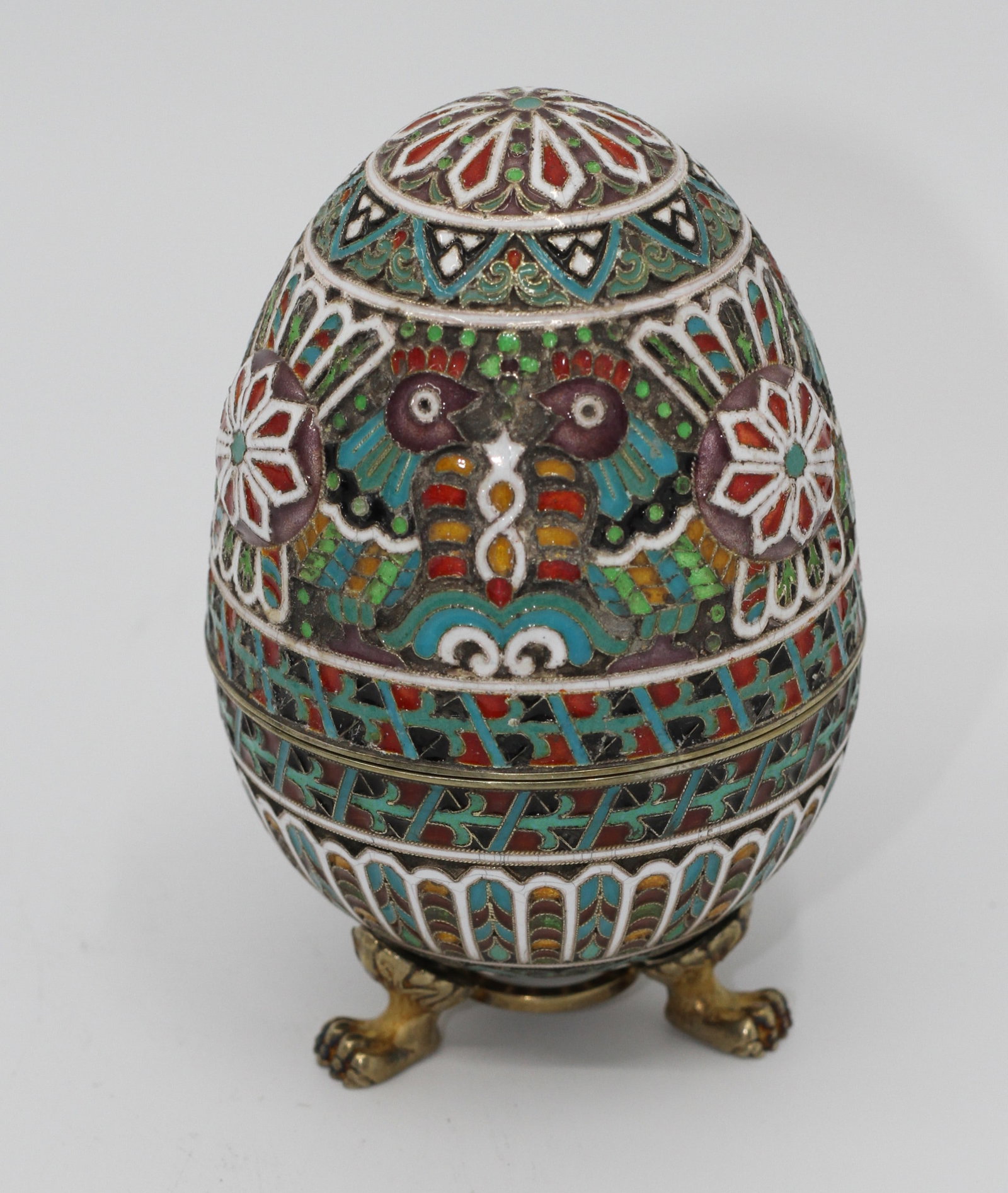 Russian Silver-Gilt Cloisonne Enamel Egg Box: Egg-form silver-gilt box raised on three paw feet, decorated throughout with colorful cloisonne enamel birds, flowers, and geometric motifs. Hinged at the center with a gilt interior. Bearing an ?84? 
